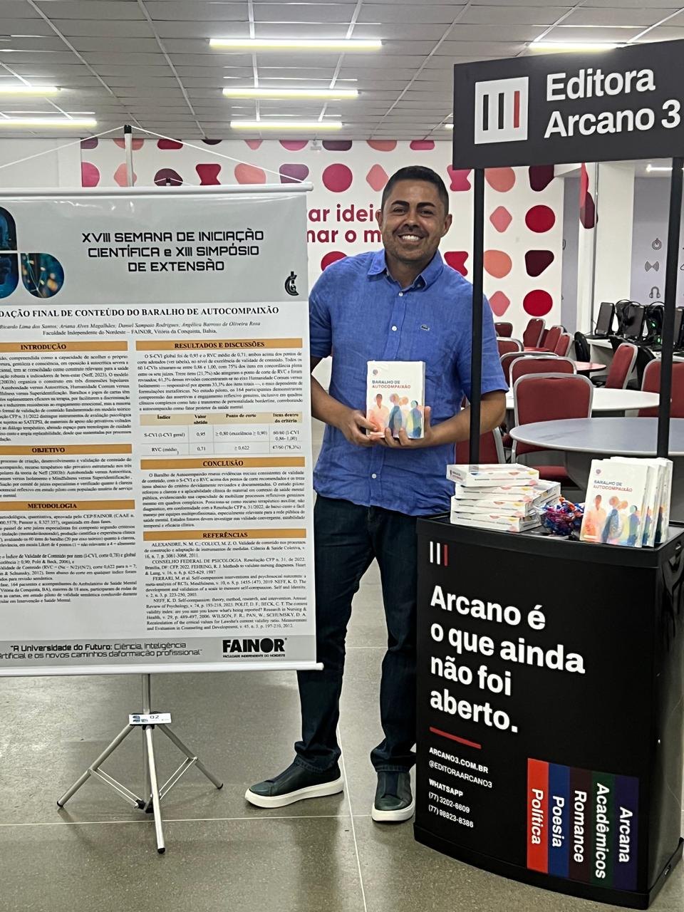 Pessoa segurando o kit do baralho ao lado do estande e do pôster