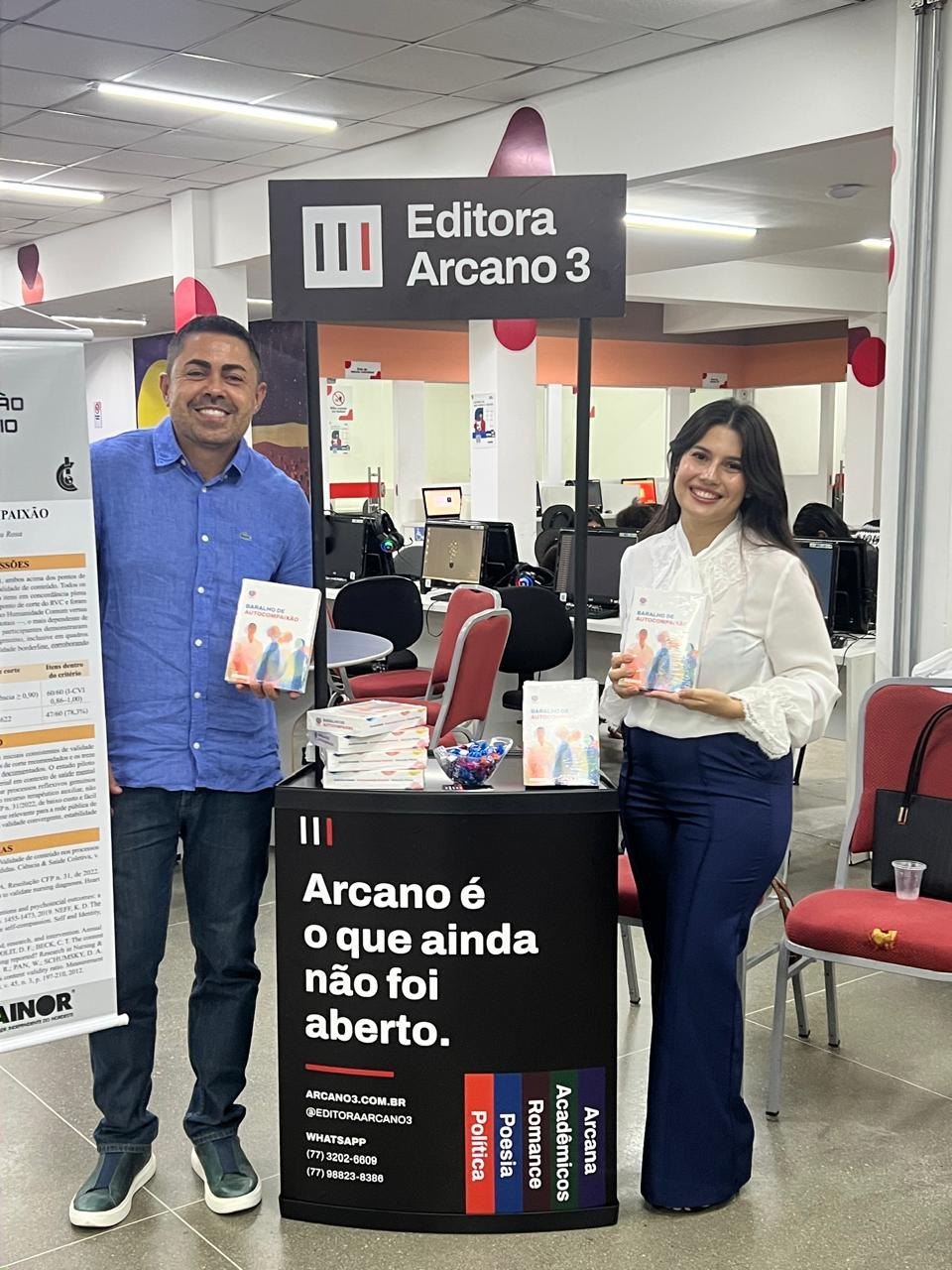 Duas pessoas com exemplares do kit junto ao estande da editora